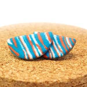 May include: A pair of blue, white and orange striped half-circle earrings. The earrings are made of polymer clay and have a unique, abstract design.