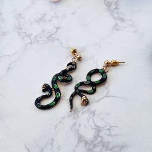 May include: A pair of gold snake earrings with black and green enamel. The snakes are curled and have a detailed design.