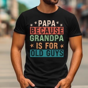 May include: Black t-shirt with a vintage-style graphic that reads "Papa Because Grandpa Is For Old Guys". The graphic features stars and colorful text.