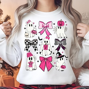 Op de afbeelding: Witte sweatshirt met een patroon van Halloween-geestillustraties. De geesten zijn versierd met strikken, hoeden en pompoenen in roze, zwart en grijs. Het ontwerp bevat ook sterren en spinnenwebben.