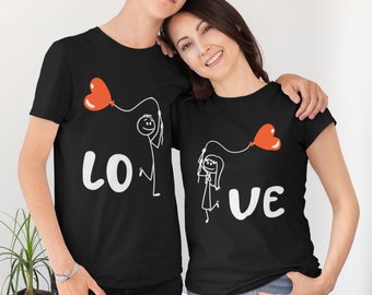 May include: Two black t-shirts with a stick figure couple holding red heart balloons. The shirts say "LO" and "VE" on them.
