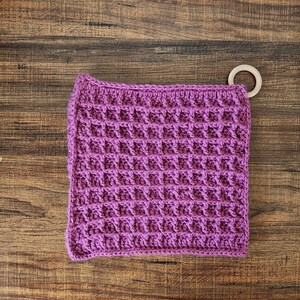 May include: Purple crocheted pot holder with a wooden ring attached.