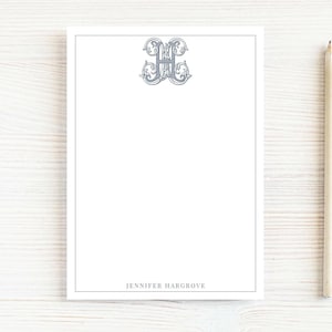 May include: A white notepad with a grey border and a decorative grey monogram at the top. The name "JENNIFER HARGROVE" is printed at the bottom. A pencil is positioned to the right of the notepad.