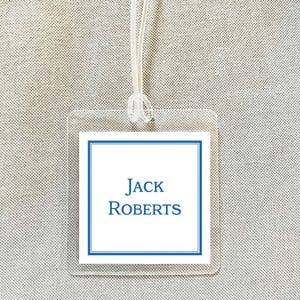 May include: Clear luggage tag with a white insert featuring the name "JACK ROBERTS" in blue text. The insert has a blue border. A clear string is attached for securing the tag.