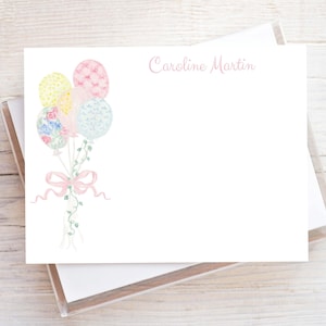May include: White stationery with a watercolor illustration of colorful balloons tied with a pink ribbon and vines. The text "Caroline Martin" is written in a delicate pink script at the top right.
