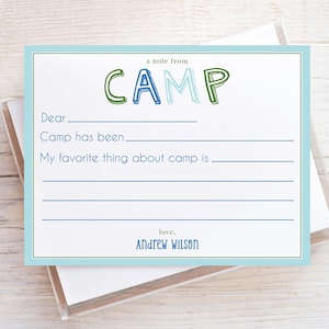 May include: A white fill-in-the-blank stationery card with a light blue border and the word "CAMP" in green and blue lettering. The card includes prompts for writing a note from camp, with the name "Andrew Wilson" at the bottom.