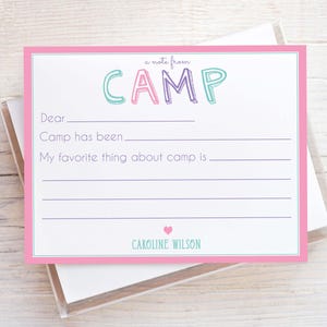 May include: A pink-framed fill-in-the-blank stationery card with the word "CAMP" in colorful letters. The card includes prompts for writing a note from camp, with a heart and the name "CAROLINE WILSON" at the bottom.