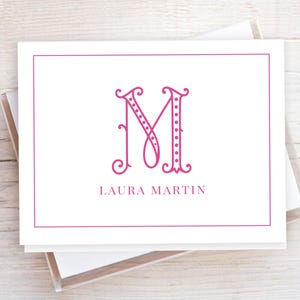 Puede incluir: Tarjeta de papelería blanca con un borde magenta y una letra "M" magenta estilizada. El nombre "LAURA MARTIN" está impreso en magenta debajo. La tarjeta es parte de un conjunto.