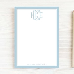 May include: A personalized stationery set featuring a light blue border and a monogram in the upper center. The name "Melissa Chandler" is printed at the bottom. A pencil rests on the side, ready for use.