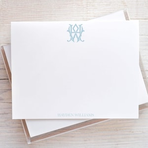 May include: White stationery set with a light blue monogram and the name "Hayden Williams" printed at the bottom. The stationery is stacked in a clear plastic box, perfect for personalized correspondence.