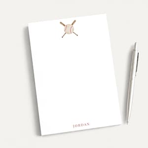 May include: A white rectangular notepad featuring a watercolor illustration of a baseball and two crossed wooden bats at the top center. The name JORDAN is printed in a dark red serif font at the bottom center, accompanied by a silver pen.