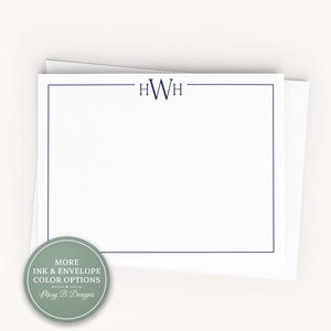 May include: A white rectangular stationery card featuring a dark blue border and the monogram HWH centered at the top. The card is placed on top of a white envelope. A circular sage green badge with the text MORE INK & ENVELOPE COLOR OPTIONS is visible.