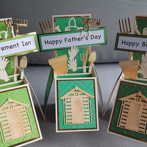 Op de afbeelding: Drie groene en gouden pop-up kaarten met een schuurontwerp. De kaarten hebben verschillende berichten: "Happy Retirement Ian", "Happy Father's Day" en "Happy Birthday Dad".
