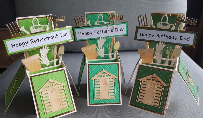 Op de afbeelding: Drie groene en gouden pop-up kaarten met een schuurontwerp. De kaarten hebben verschillende berichten: "Happy Retirement Ian", "Happy Father's Day" en "Happy Birthday Dad".