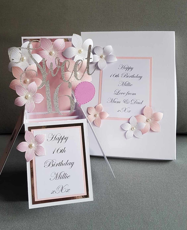 May include: A pink and white pop-up card with a silver glitter "Sweet 16" design. The card has a pink balloon and flowers. The card reads "Happy 16th Birthday Millie Love from Mum & Dad xxx".