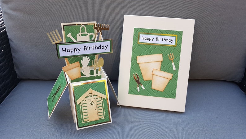 Op de afbeelding: Een groene en gouden pop-upkaart met een tuinmotief. De kaart toont een klein schuurtje, tuingereedschap en de tekst "Happy Birthday".