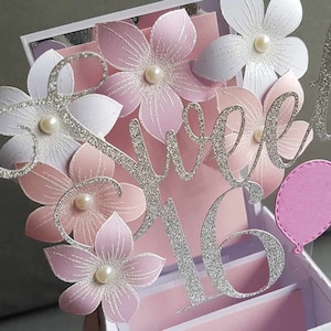 May include: A silver glitter card with the words "Sweet 16" and pink flowers. The card is decorated with white pearls and a pink balloon.