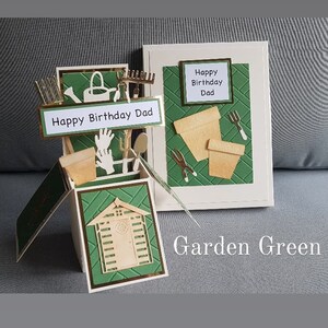Op de afbeelding: Een groene en gouden pop-upkaart met een schuur, tuingereedschap en de tekst "Happy Birthday Dad" en "Garden Green".