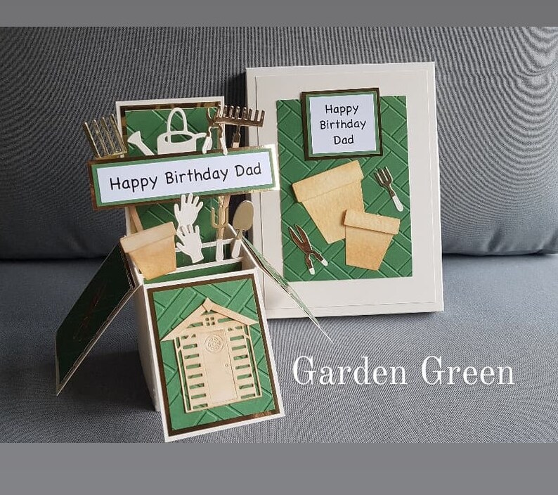 Op de afbeelding: Een groene en gouden pop-upkaart met een schuur, tuingereedschap en de tekst "Happy Birthday Dad" en "Garden Green".