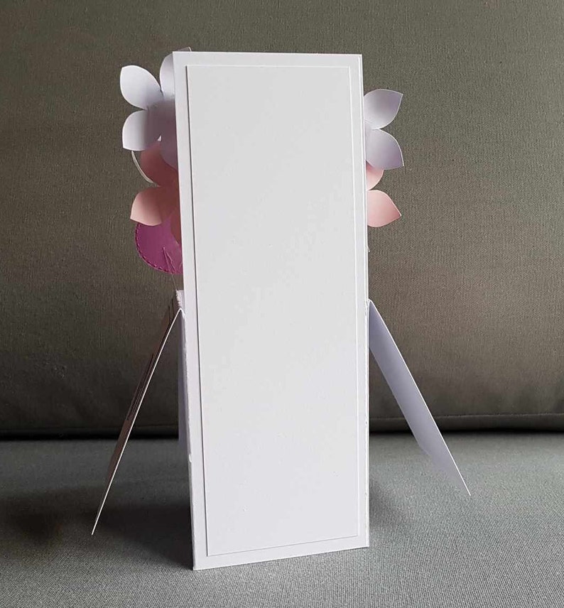 May include: A white card with a blank front and a decorative floral design on the back. The flowers are pink, purple, and white.