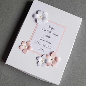 May include: A white card with pink trim and pink and white flowers. The card says "Happy 16th Birthday Millie Love from Mum & Dad xx".