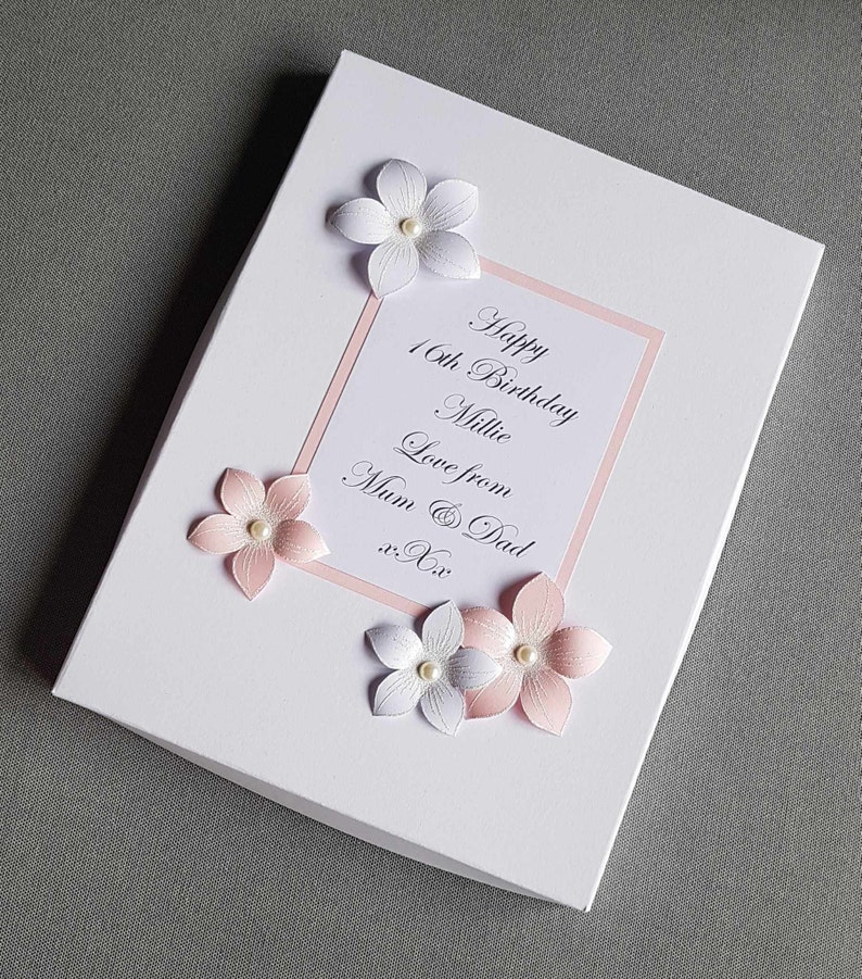May include: A white card with pink trim and pink and white flowers. The card says "Happy 16th Birthday Millie Love from Mum & Dad xx".