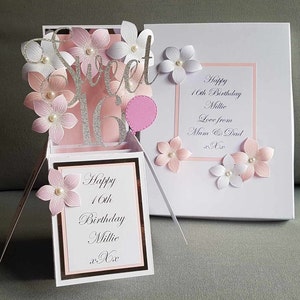 May include: A pink and white pop-up card with a silver glitter 'Sweet 16' design. The card has a pink balloon and flowers. The inside of the card says 'Happy 16th Birthday Millie xx'.
