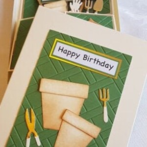 Op de afbeelding: Een groene en witte kaart met een pop-up ontwerp. De kaart heeft een tuin thema met een pot, een schop en een schaar. De kaart zegt "Happy Birthday" op de voorkant.
