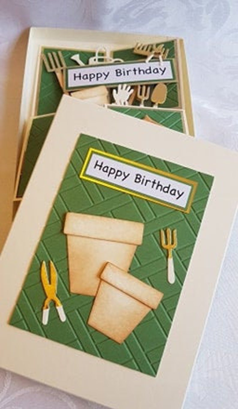 Op de afbeelding: Een groene en witte kaart met een pop-up ontwerp. De kaart heeft een tuin thema met een pot, een schop en een schaar. De kaart zegt "Happy Birthday" op de voorkant.