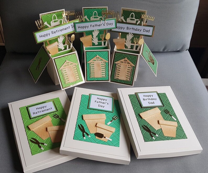Op de afbeelding: Drie witte kaartdozen met groene en gouden accenten. De dozen zijn versierd met een tuiniersthema en hebben de tekst "Happy Retirement", "Happy Father's Day" en "Happy Birthday Dad" op de voorkant.