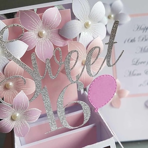 May include: A silver glitter 'Sweet 16' pop-up card with pink and white paper flowers and a pink balloon. The card has a white background with a pink border and the text 'Happy 16th Birthday Millie Love from Mum & Dad xxx'.