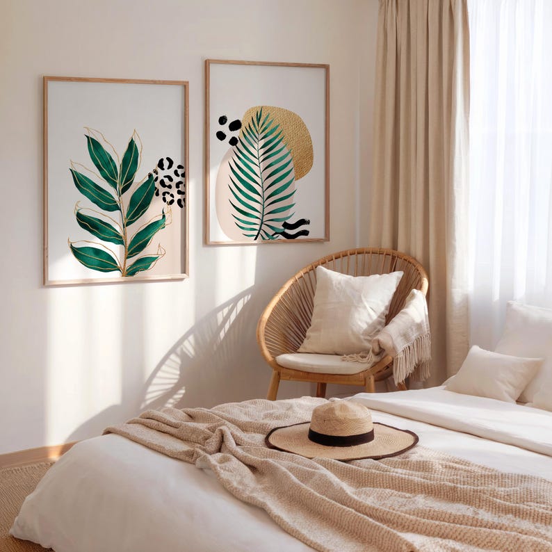 May include: Two framed botanical art prints with green leaves and gold accents. One print features a large green leaf design, and the other has a gold sun shape and a green leaf. The prints are displayed above a bed with a straw hat.