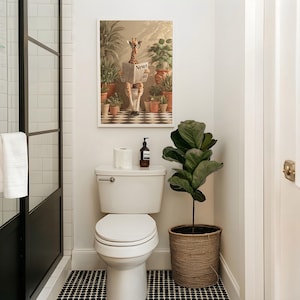 a bathroom with a toilet, a framed picture of a giraffe reading a newspaper, and a potted plant.