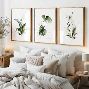 a cozy and well-decorated bedroom with a large bed, white bedding, and three framed botanical prints hanging on the wall above it.