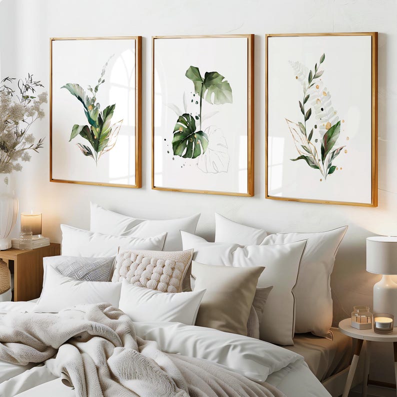 a cozy and well-decorated bedroom with a large bed, white bedding, and three framed botanical prints hanging on the wall above it.