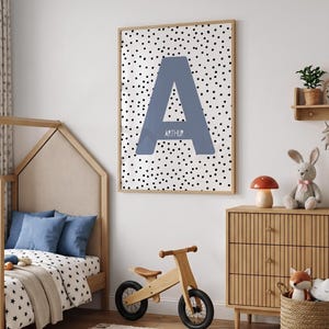 May include: A rectangular wall art print in a light wood frame featuring a large, slate blue capital letter A centred on a white background with a black polka dot pattern. The name ARTHUR is printed in white, sans-serif text across the letter A.