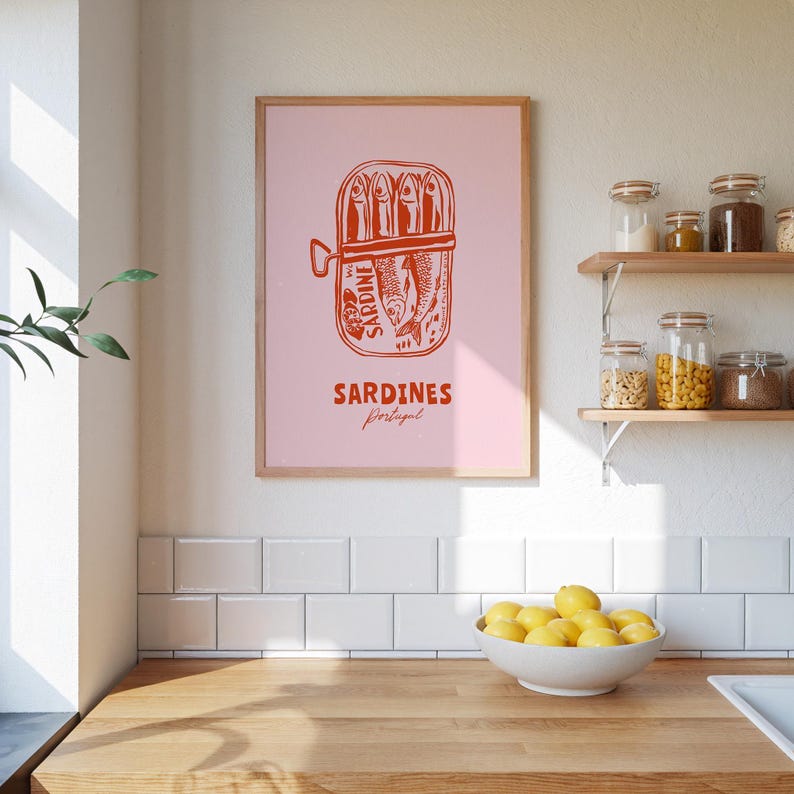 a kitchen counter with a bowl of lemons, a framed poster of a can of sardines, and shelves with various jars and containers.
