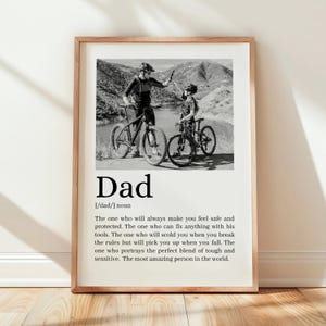 May include: Black and white framed print featuring a photograph of a father and child on bicycles. The word "Dad" is printed in large, bold letters below the photo, along with a definition.