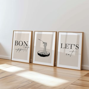 Puede incluir: Tres impresiones artísticas enmarcadas con fondo beige y marcos de madera. Las impresiones presentan dibujos lineales negros de pasta, un tenedor y las frases "BON appétit" y "LET'S eat". La obra de arte se exhibe sobre un suelo de madera clara.