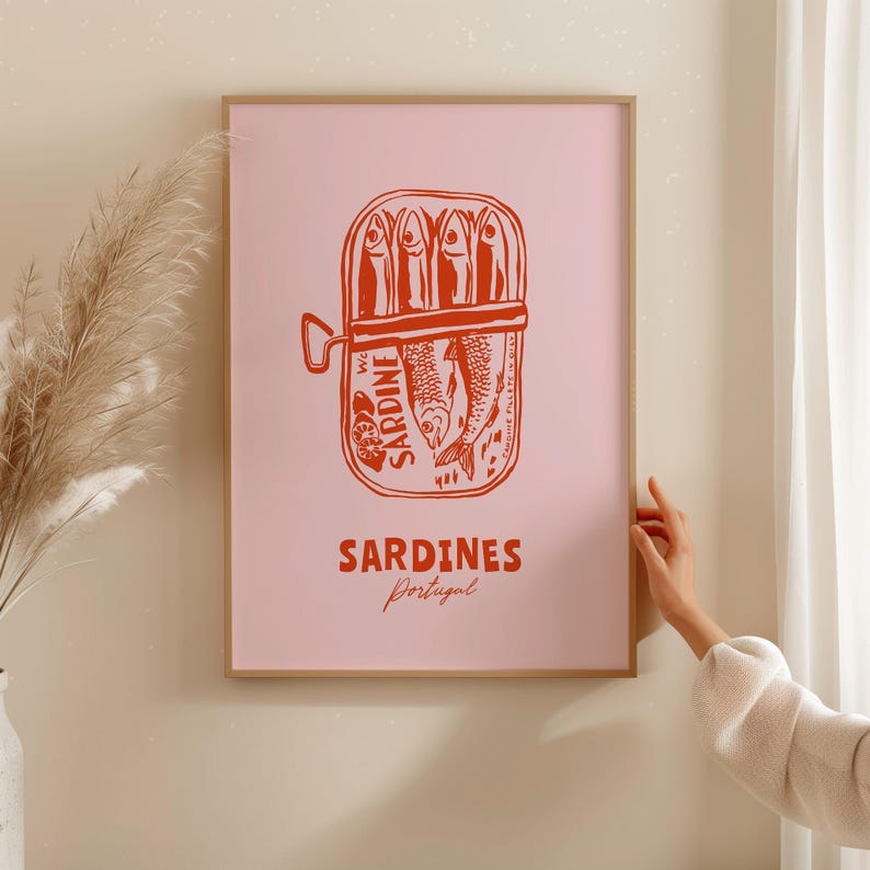 A framed poster of a can of sardines is hanging on a wall, with a person's hand reaching towards it.