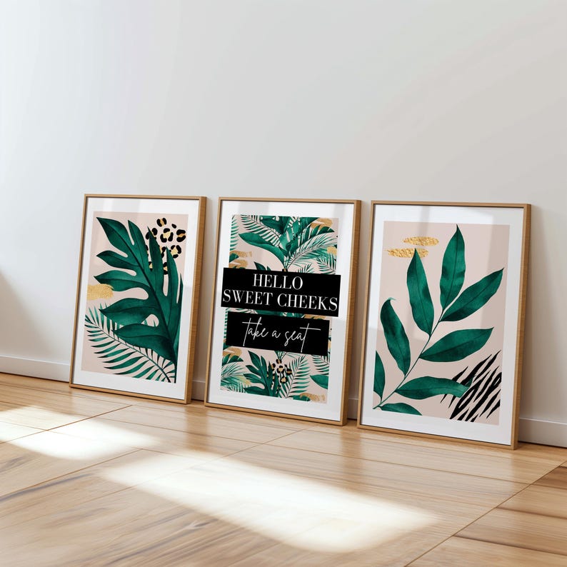 Three framed prints with tropical plant designs are displayed on a wooden floor against a white wall.