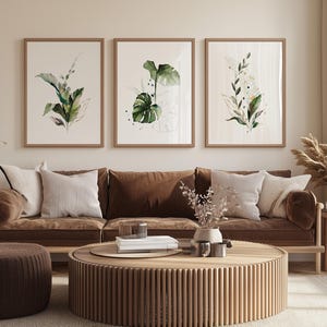 a cozy living room with a brown sofa, a round wooden coffee table, and three framed botanical prints on the wall above the sofa.