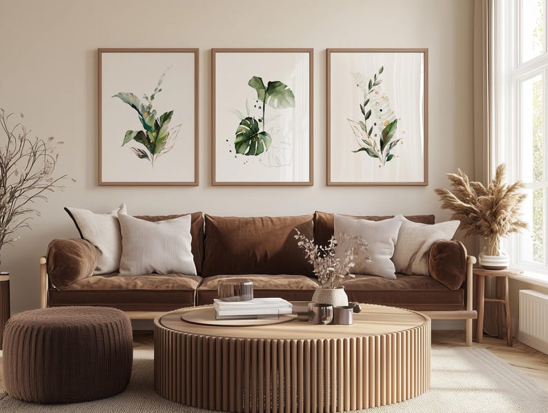 a cozy living room with a brown sofa, a round wooden coffee table, and three framed botanical prints on the wall above the sofa.