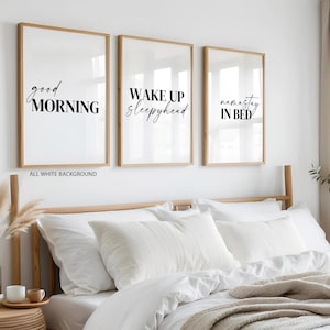 Puede incluir: Tres impresiones artísticas enmarcadas con marcos de madera. Las impresiones tienen un fondo blanco con texto negro que dice "good MORNING", "WAKE UP sleepyhead" y "namastay IN BED". Las impresiones están encima de una cama con ropa de cama blanca.