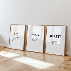 Könnte beinhalten: Drei rechteckige Wandbilder in hellen Holzrahmen. Jedes weiße Bild enthält schwarzen Text. Das erste zeigt STAY positive, das zweite WORK hard und das dritte MAKE IT happen, wobei eine Kombination aus fetten Block- und Schreibschriften verwendet wird.