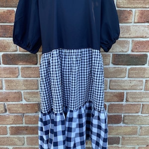 May include: A black and white gingham dress with a black bodice and a tiered skirt. The dress has a round neckline and short puff sleeves.