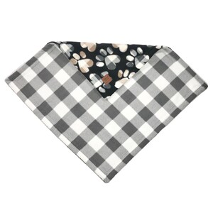 Puede incluir: Una manta reversible para perros con un patr&oacute;n de cuadros de b&uacute;falo blanco y negro en un lado y un vell&oacute;n negro con huellas de patas y corazones en el otro lado.
