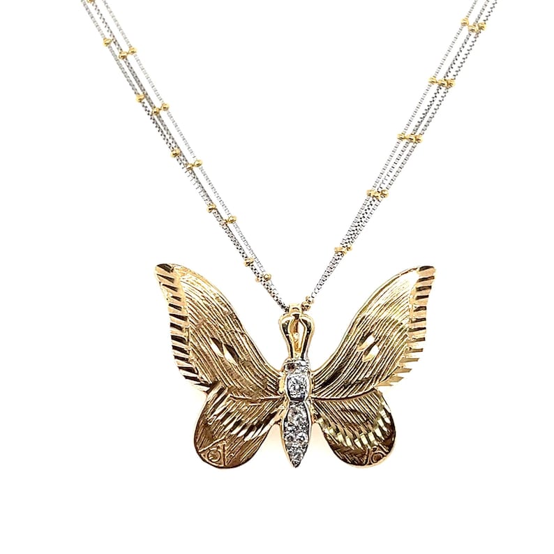 May include: A gold-coloured butterfly pendant necklace with a dual-strand chain. The butterfly has detailed wing patterns and a small cluster of clear stones at the centre. The necklace has a delicate, elegant design.