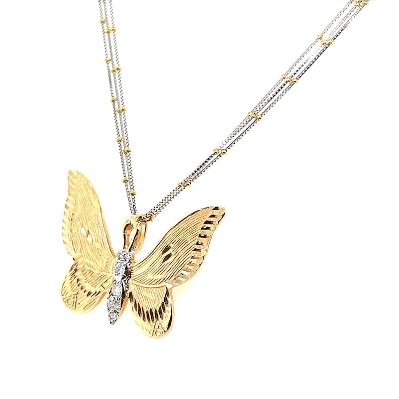 May include: A gold butterfly pendant necklace with a fine chain. The butterfly features detailed wing patterns and a line of small, sparkling stones. The necklace is displayed against a white backdrop.