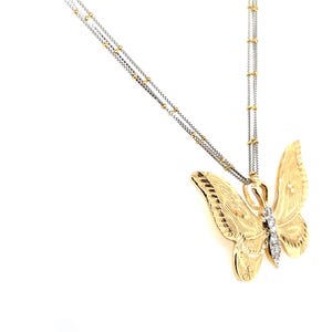 May include: A gold-coloured butterfly pendant necklace with a textured finish. The butterfly has a diamond accent and hangs from a delicate chain. The necklace is a jewellery item.